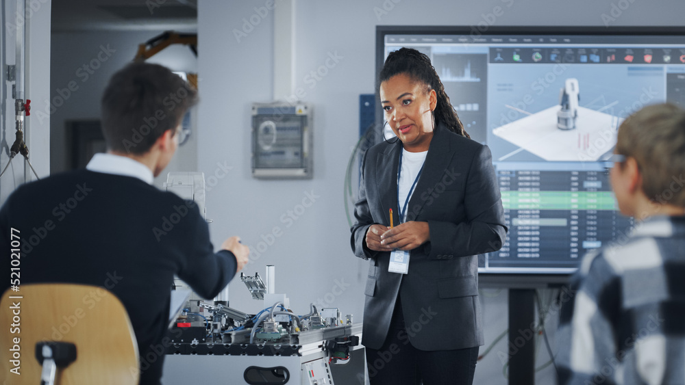 Fototapete Black Teacher Asking at Students Questions and Pointing at Robotic Hand while Explaining During Lesson. Smart Boy Pointing With Hand at Robot. Engineering and Programming Language Concept.