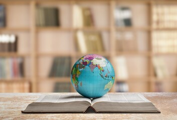 Old globe lying on an open book against the background of bookshelves in a library. Science, education, travel. Education history and geography team.