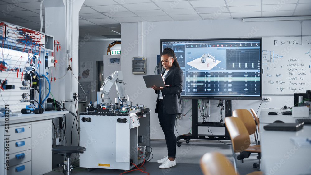 Poster Black Female Automation Engineer Holding Laptop and Moving Bionic Arm With Written Code at Futuristic Factory. Modern Equipment and New Era in Computer Science and Robotics Industry Concept.