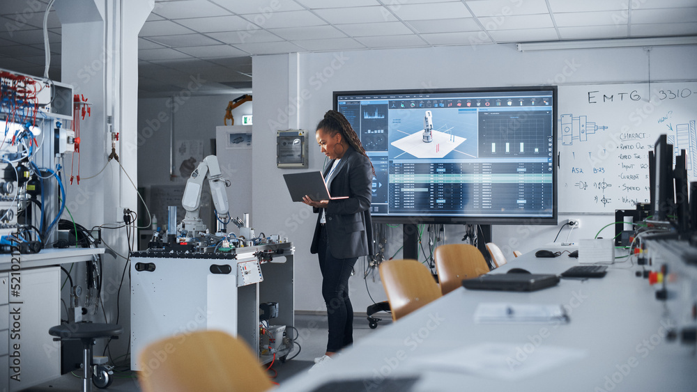 Aufkleber Black Female Automation Engineer Holding Laptop and Moving Bionic Arm With Written Code at Futuristic Factory. Modern Equipment and New Era in Computer Science and Robotics Industry Concept.