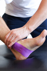 Kinesiology taping treatment with purple tape on male patient injured foot. Sports injury kinesio...