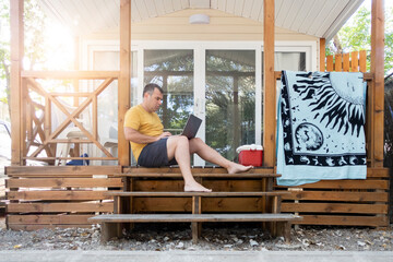 a man sitting on the porch of a cabin working on a laptop computer while on vacation
