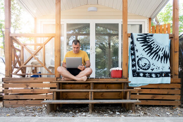 a man sitting on the porch of a cabin working on a laptop computer while on vacation