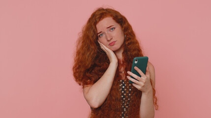 Unhappy sad young redhead woman use smartphone typing browsing, loses becoming surprised sudden...