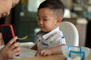 Cute Asian baby boy sitting in a high chair eating rice.