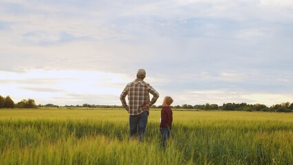 Fototapeta na wymiar Farmer and his son in front of a sunset agricultural landscape. Man and a boy in a countryside field. Fatherhood, country life, farming and country lifestyle.
