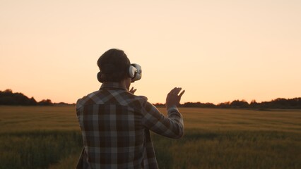 Farmer in virtual reality helmet in front of a sunset agricultural landscape. Man in a countryside field. Country life, food production, farming and technology concept