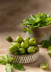 Fresh gooseberry in ceramic bowl with mint leaves on beige textured background with copy space. Close up. Raw healthy dessert.