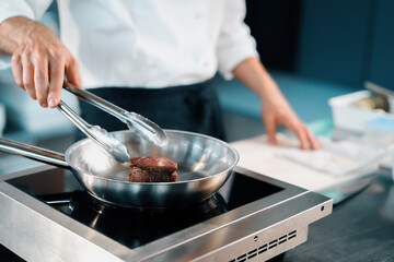 Professional restaurant kitchen, close-up: male chef preparing filet mignon on a frying pan