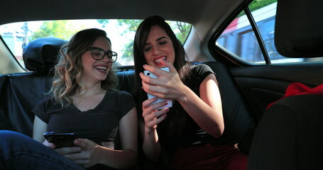 Real life laugh of friends together in the back seat of a taxi holding cellphones and checking...