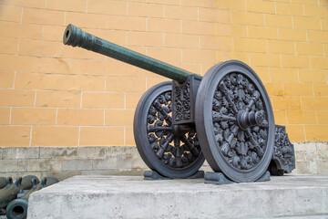 A bronze cannon on a carriage located on a white stone pedestal near the arsenal building in the...