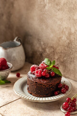 Chocolate cake with red summer berries sprinkled with powdered sugar on beige tile background. Beautiful still life, text space