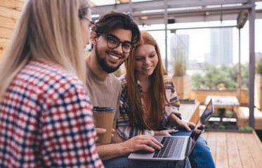 Group of diverse students brainstorming on university project while sitting at campus with laptop computer. Three friends learning together and discussing online information on netbook