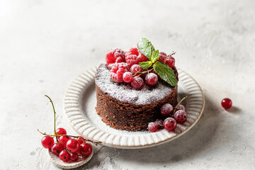 Chocolate cake with red berries, mint leaves and snowy powdered sugar close up on white textured background