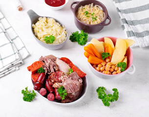 Cocido madrileno, traditional Spanish hot meal with assorted stewed meat, vegetable, chickpea and noodles served separately on the white table