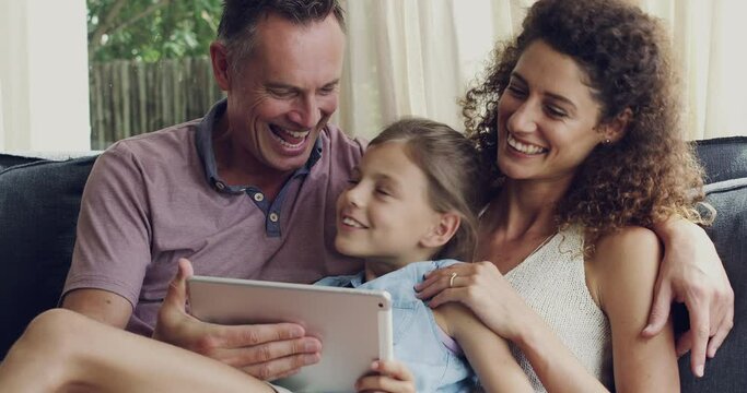 Happy, loving and cheerful family browsing for a movie online on a tablet while sitting and bonding together on their couch at home. Mother, father and daughter relaxing streaming fun videos indoors