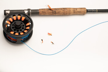 Fly fishing reel, rod, and flies on a white wood background with copy space