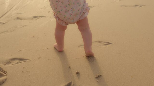 Closeup feet baby learns to walk on beachside on sand unknown barefoot kid toddler child unrecognizable daughter son make first steps learning walking on beach at summer going clumsily hot sandy coast