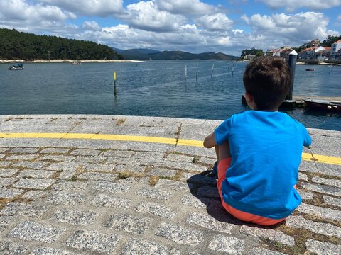 young kid looking at the boats working with clams near cortegada island. Relaxed Young boy close to the sea