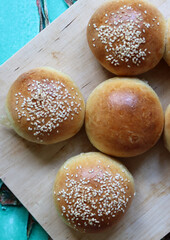 Home baked buns with sesame seeds on wooden board. Close up photo of crusty sourdough buns. 