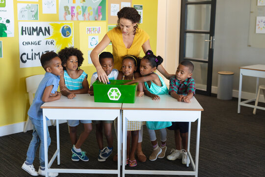 Caucasian young female teacher and african american elementary students with recycling container
