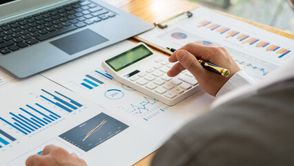 An accountant, businessman or financial professional presses calculators, computes, analyzes graphs, business reports, and financial charts at the office. economic concepts, finance, market research