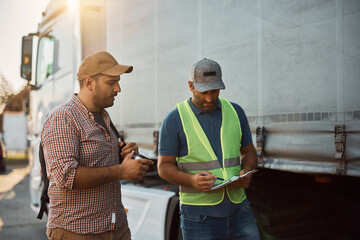 Freight transportation manager and truck driver going through checklist on parking lot.