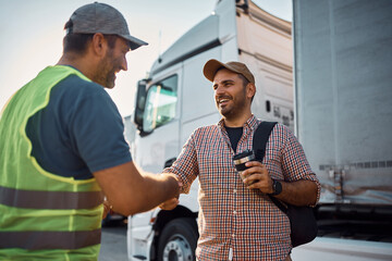 Happy truck driver and freight transportation manager greeting on parking lot.