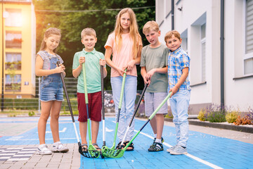 Group of children playing street hockey on a city holiday on the playground. Portrait of group of five different age kids hockey ball player with hockey stick.