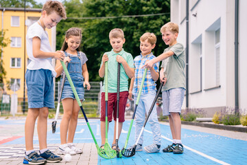 Group of children playing street hockey on a city holiday on the playground. Portrait of group of five kids hockey ball player with hockey stick.