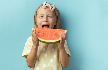Cute little girl enjoying big slice of juicy red watermelon on the blue background. Portrait of happy caucasian girl with blonde hair in a yellow t-shirt. Hot summer concept
