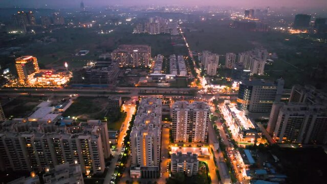 aerial drone shot moving to the side showing brightly lit orange streets with skyscrapers, towers housing homes offices and shopping complexes in between with the city skyline in the distance in