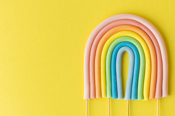 Cartoon edible rainbow made of confectionery mastic on the yellow background. Multicolored cake topper. Decoration for a cake