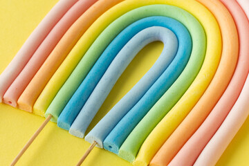 Cartoon edible rainbow made of confectionery mastic on the yellow background. Multicolored cake topper. Decoration for a cake