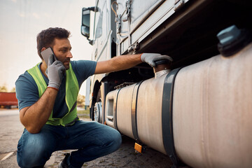 Truck driver talking on cell phone while checking gas tank on parking lot.