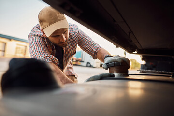 Professional truck driver checking gas tank on parking lot.