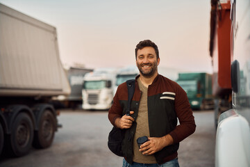 Happy truck driver with takeaway coffee on parking lot looking at camera.