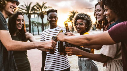 Happy multiracial friends toasting beer bottles together outside - Group of young people having...