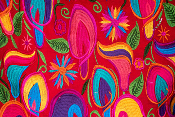 Colorful handmade fabric from Chiapas, Mexico.  Flowers edged in various colors on a red background.
