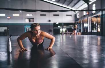 Strong Caucasian female athlete doing push ups having workout for warming up muscles, determined fit girl reaching fitness goals exercising in gym studio training body and physical strength