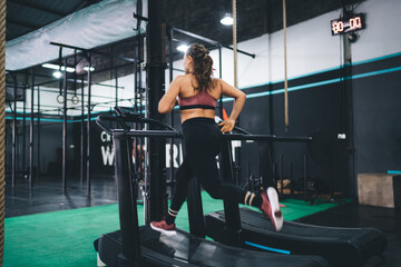 Muscular female jogger in tracksuit running at treadmill simulator - training power and endurance,...