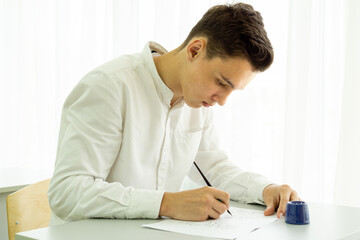 A student learns to write with a fountain pen at a white table. Back to school concept, exams,...