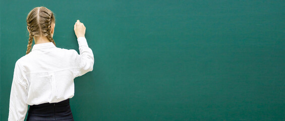 A schoolgirl standing in a classroom at a green blackboard with a place for text. High quality photo © Катерина Решетникова