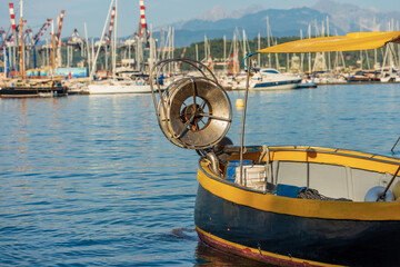 Small yellow and black fishing boat with a winch for fishing with nets, moored in the port of La Spezia town, Gulf of La Spezia, Mediterranean sea, Liguria, Italy, Europe. - obrazy, fototapety, plakaty