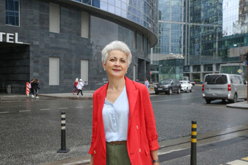 an elegant woman with gray hair in a red jacket on a city street