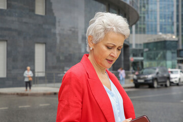 an elegant woman with gray hair in a red jacket on a city street