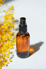 Amber pump bottle with serum, tonic or essential oil with yellow flowers. White background with daylight. Beauty concept for face and body care