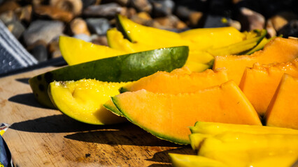Image of mango and melon slices on the beach. Picnic summer vibes.