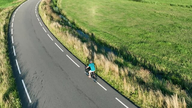 Man cycling on a winding country road during sunset seen from above. The drone is following the cyclist.