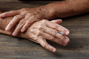 Elderly wrinkled woman hands with a cigarette on wooden table. Concepts of women's health, bad habits, lung cancer disease. Shallow depth of field